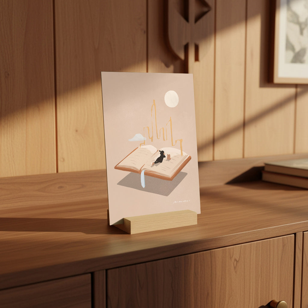 Mini print with a design of a girl on an open book, placed on a wooden surface.