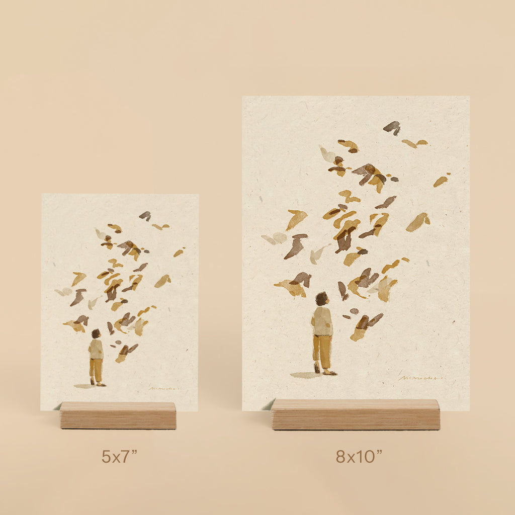 Two prints of a man and child with birds on beige backgrounds, displayed on stands.