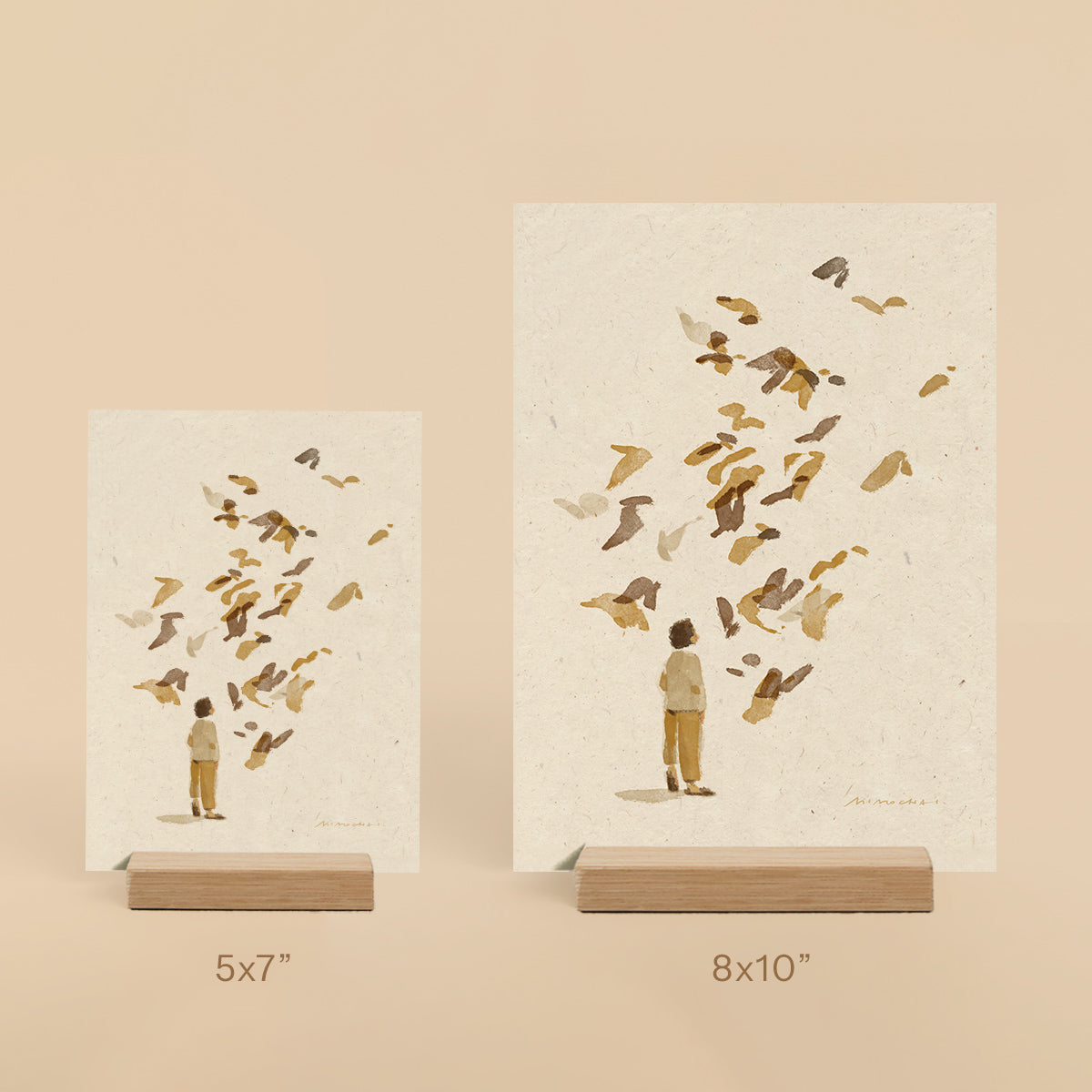 Two prints of a man and child with birds on beige backgrounds, displayed on stands.