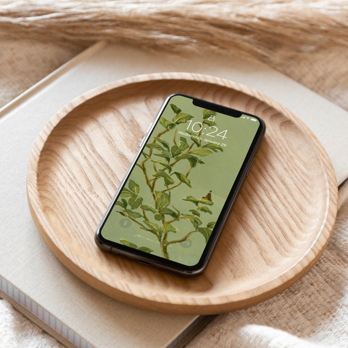 Smartphone with a nature-themed Camellia Leaves wallpaper on a wooden plate