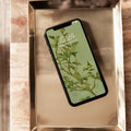 Smartphone with a green leafy pattern on the screen displayed on a metallic surface.