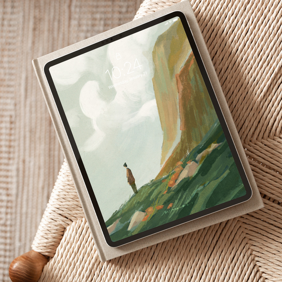 Tablet displaying a scenic landscape with a person on a grassy hill, placed on a textured surface.