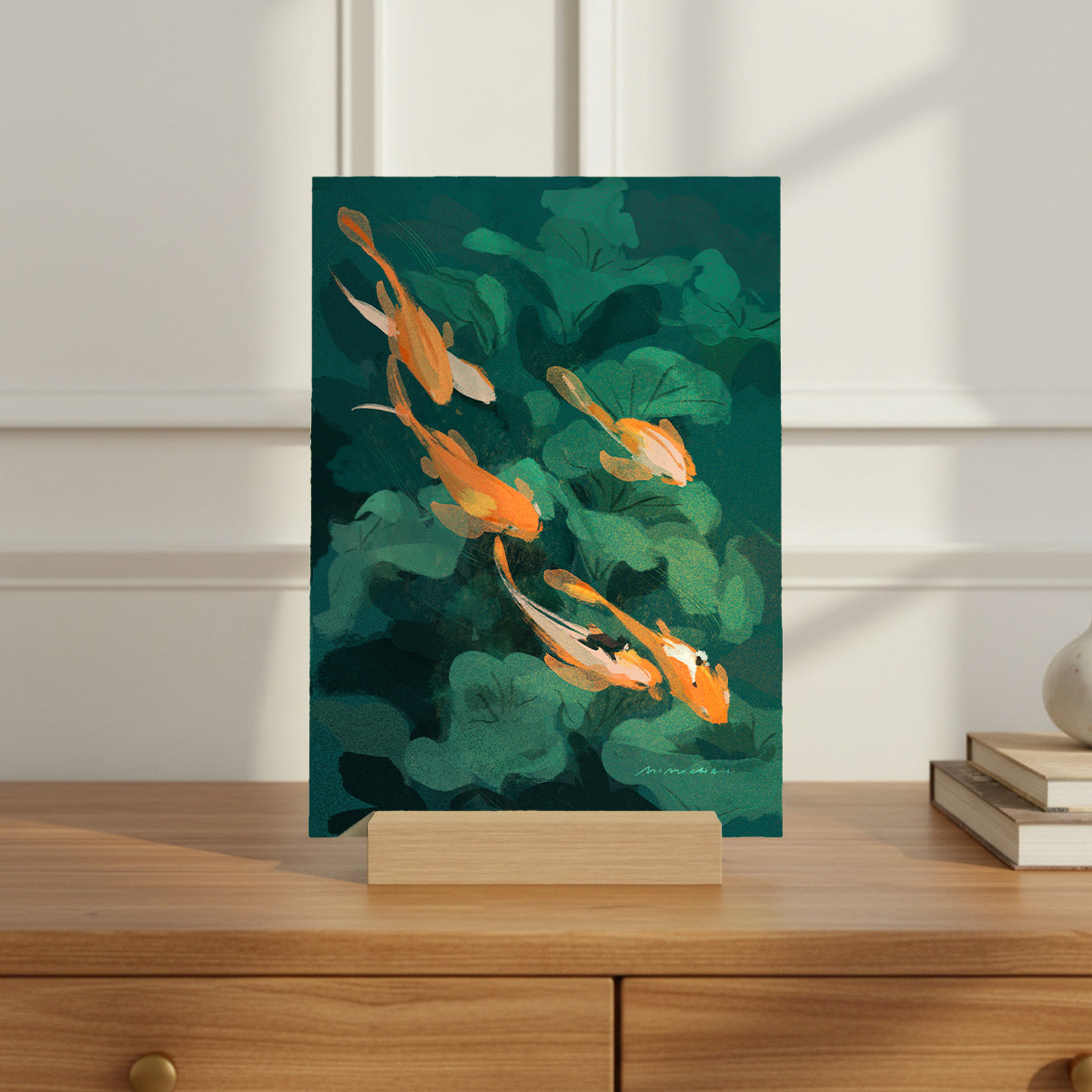Art print of goldfish and green leaves on a wooden stand against a white wall.