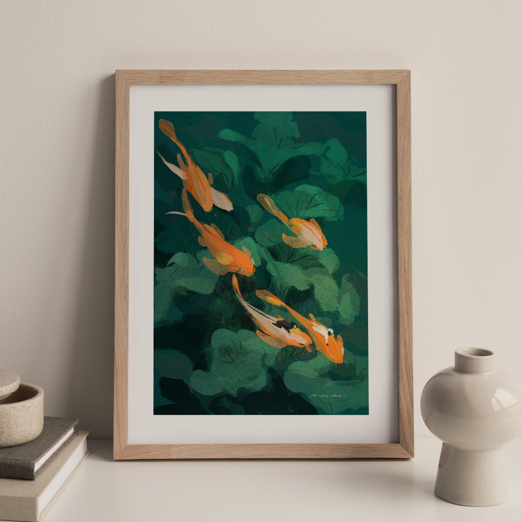 Framed artwork of a goldfish and green leaves against a beige wall. 