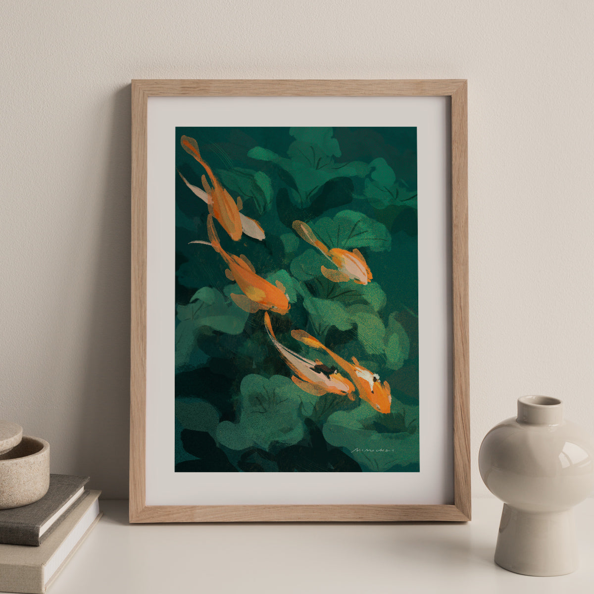 Framed artwork of a goldfish and green leaves against a beige wall. 