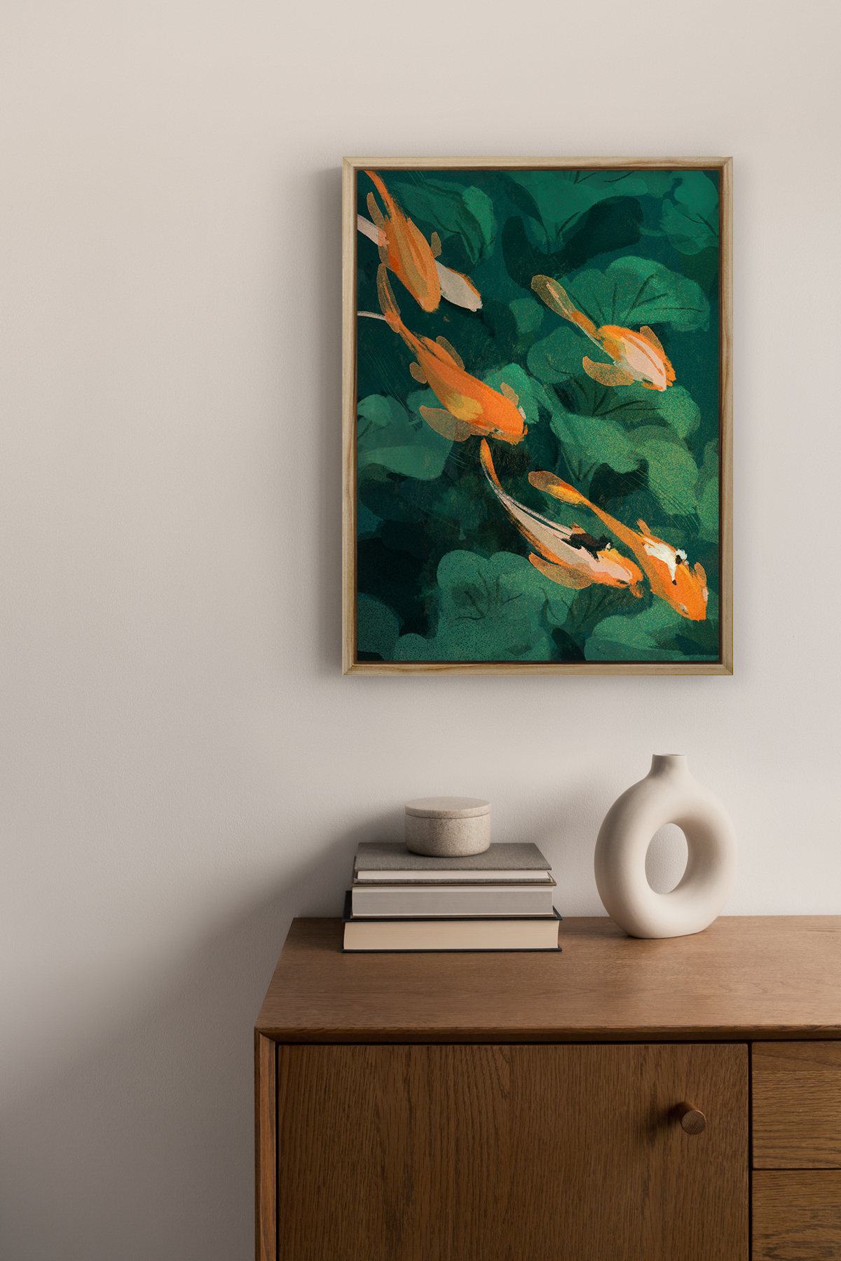Framed canvas print of goldfish and green leaves on a beige wall above a wood credenza. 