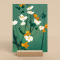 Floral artwork with white and orange flowers on a green background, displayed on a wooden stand.