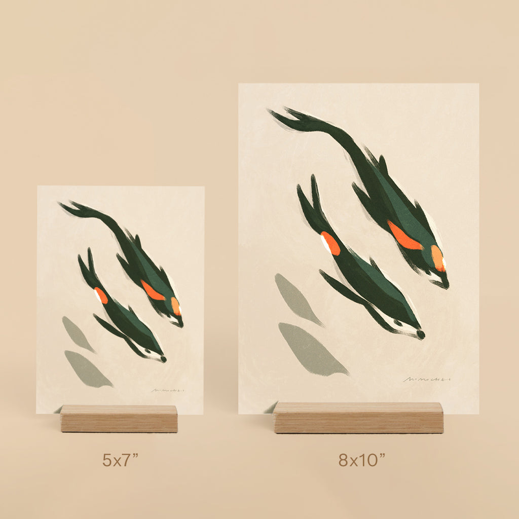 Two art prints of koi fish on beige backgrounds with wooden stands.