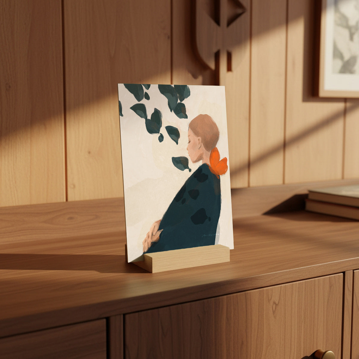 Small framed artwork of a woman with leaves on a wooden surface