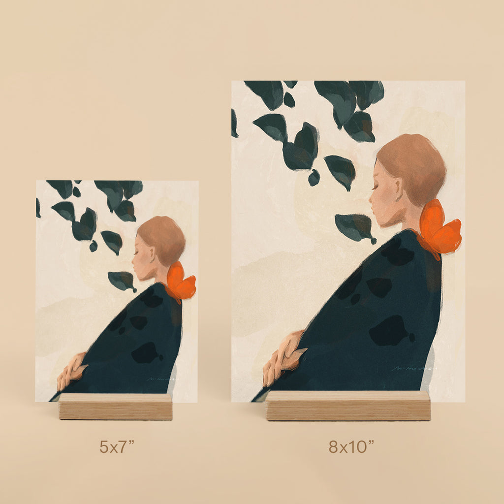 Two art prints of a woman with an orange butterfly on her shoulder on a beige background.