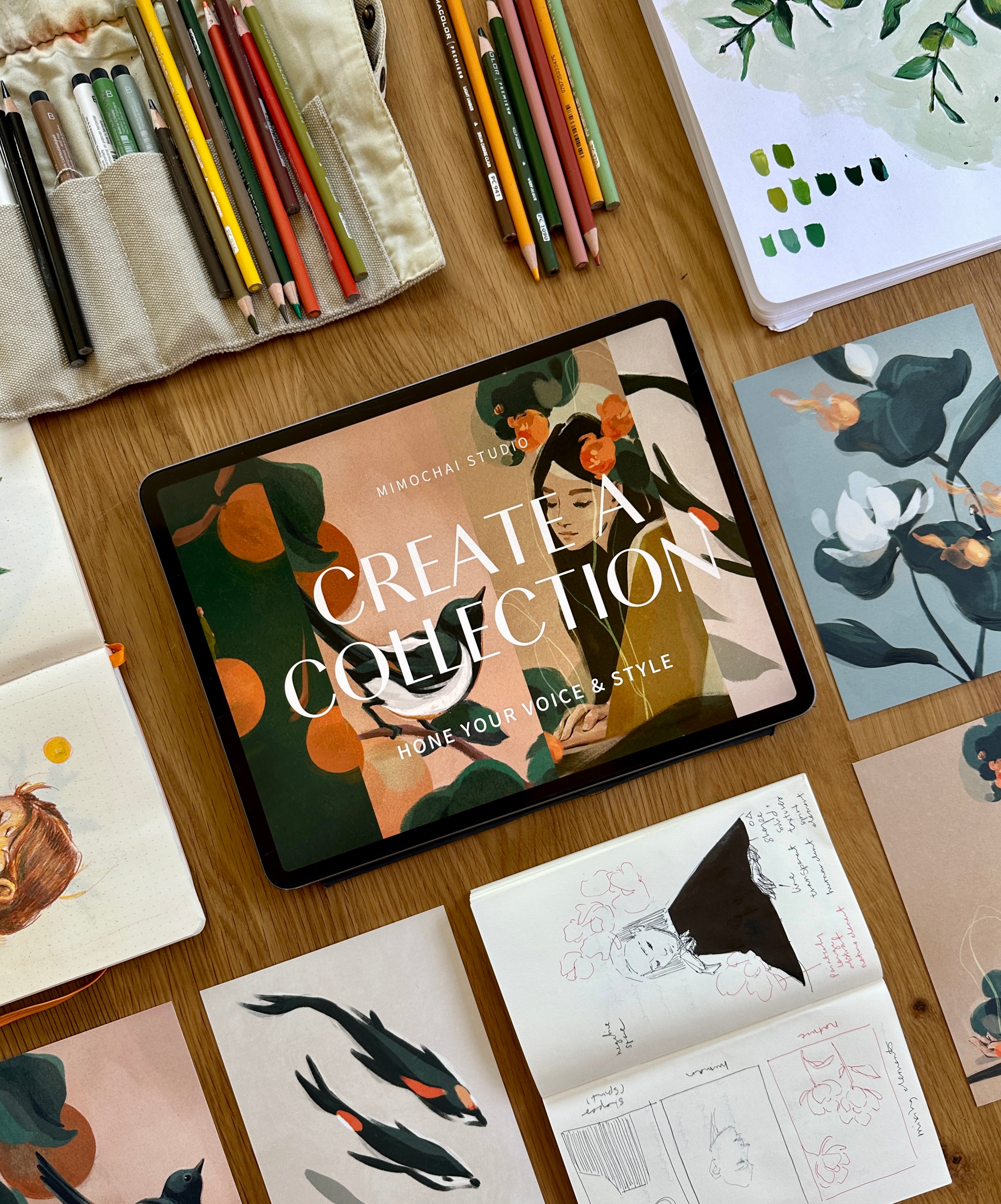 A photo of a desk with an iPad, notebooks, artwork, and colored pencils. 