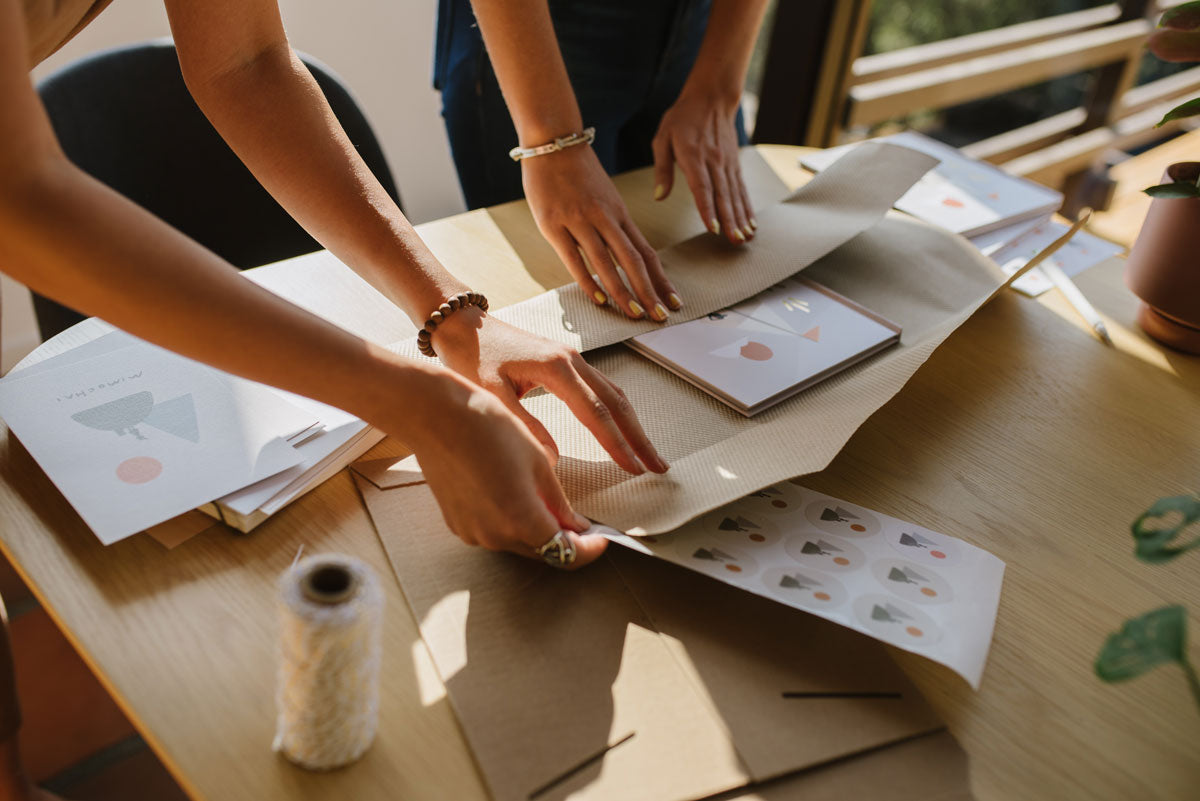 Two people shipping Mimochai products table with materials and tools.