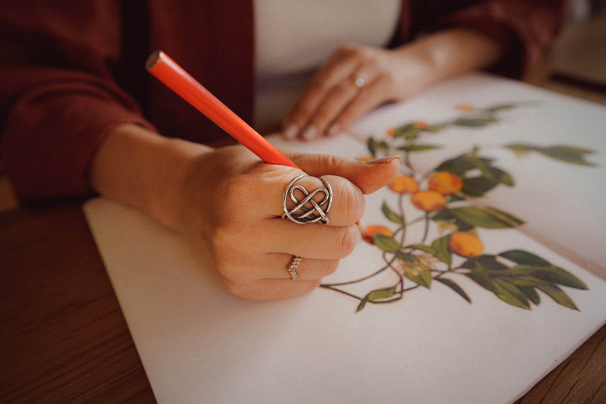 A woman's hand using colored pencils to draw oranges and leaves in a sketchbook