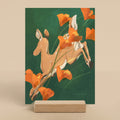 Art print of a deer among orange poppies on a green background, displayed on a wooden stand.