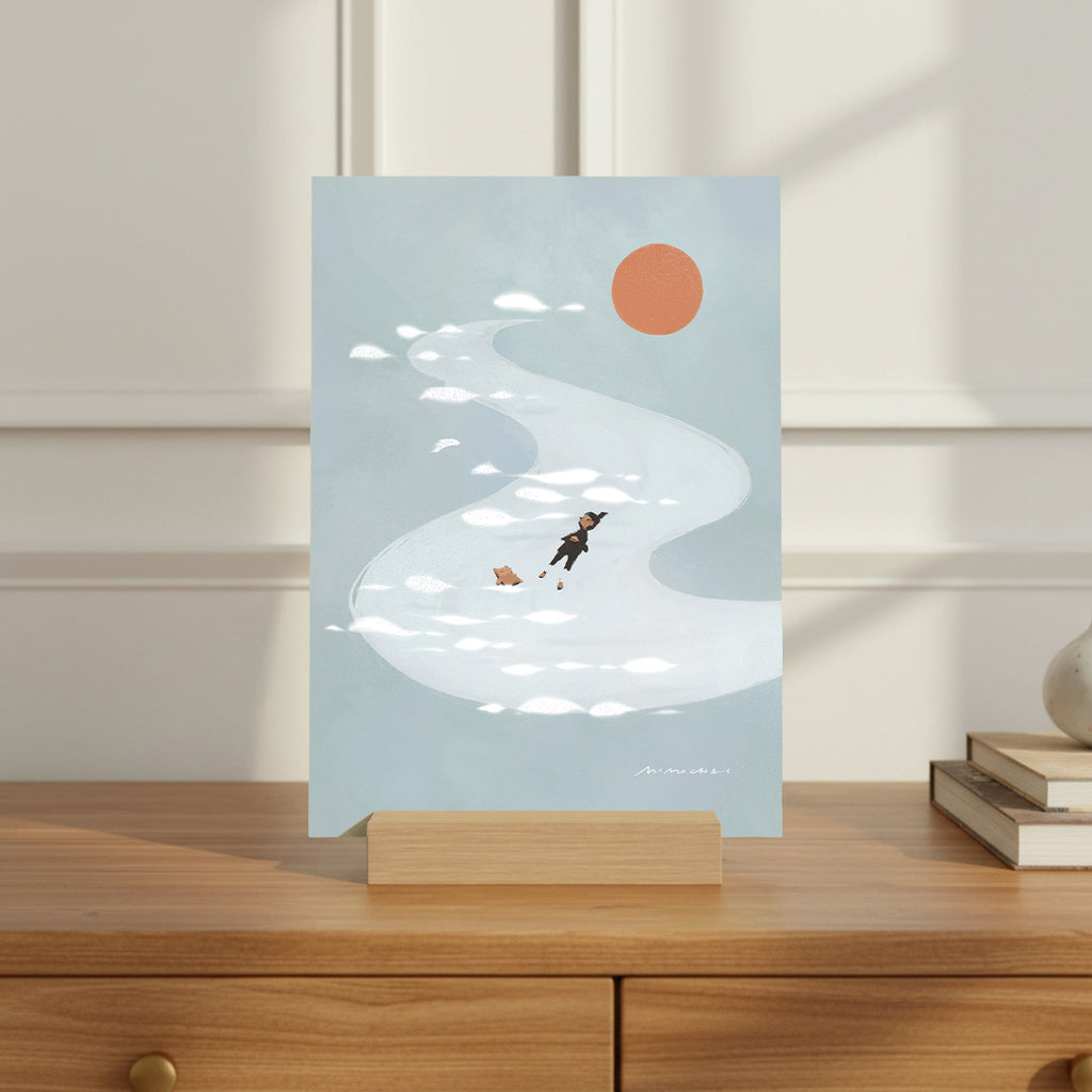 Illustrated card with a person and dog floating in a river under a red sun, placed on a wooden surface.