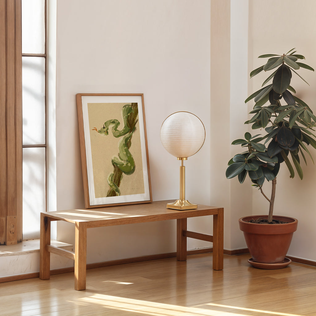 Room interior with a wooden bench, framed artwork, table lamp, and potted plant.