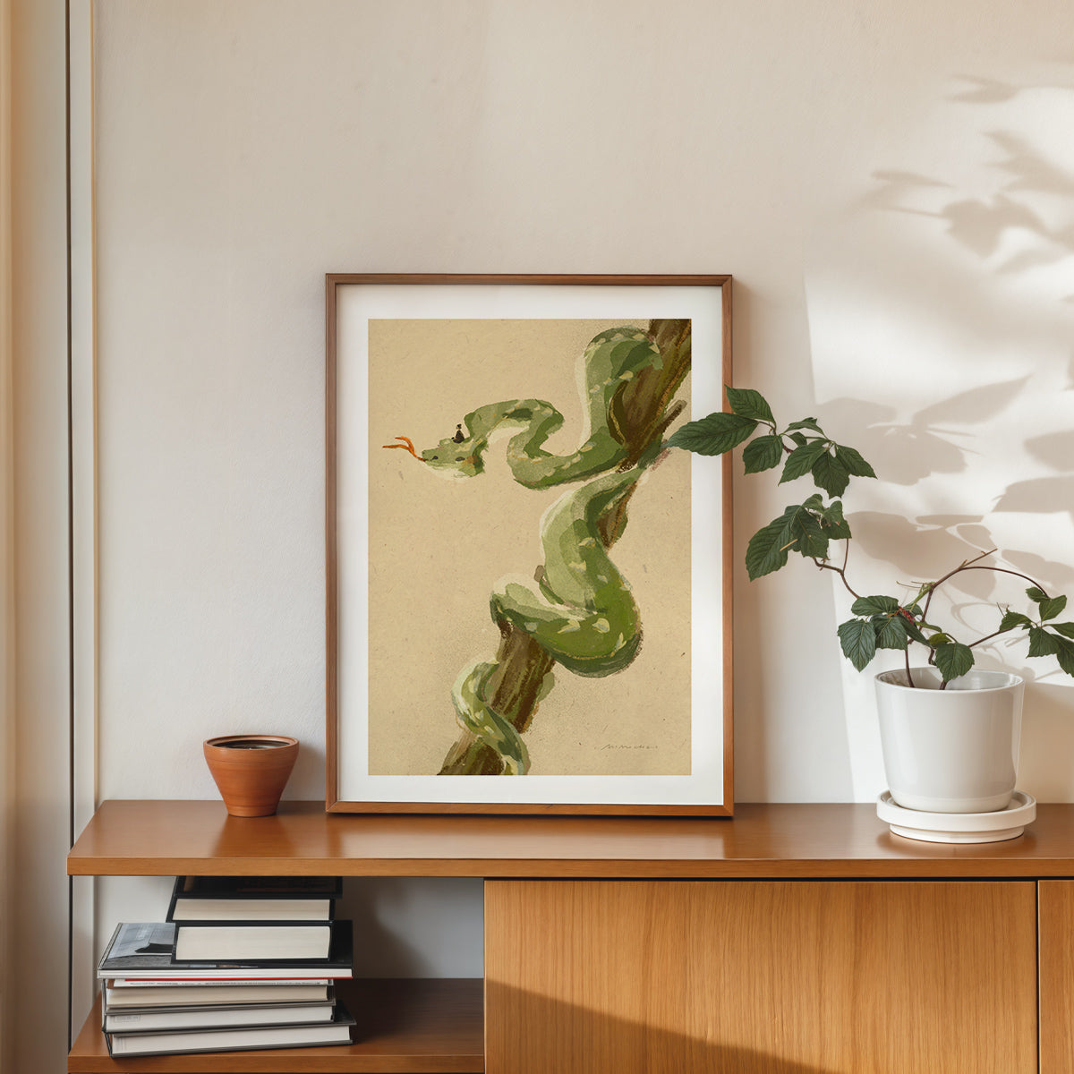 Framed artwork of a green snake on a wooden shelf with books and a plant.