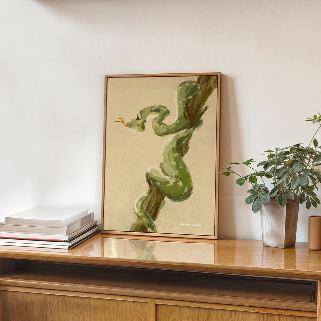Framed artwork of a green snake on a wooden shelf with books and a plant.